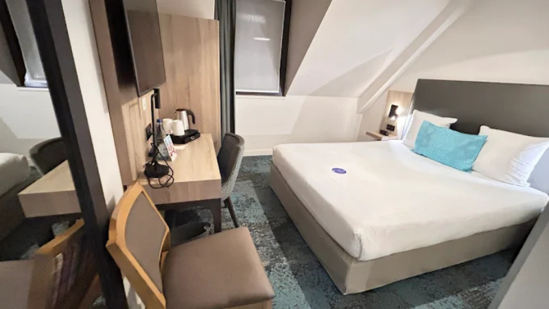 Modernt hotellrum på Hotel Turenne i Colmar med dubbelsäng, skrivbord, stol, platt-TV och kaffekokare i ljus och kompakt design.